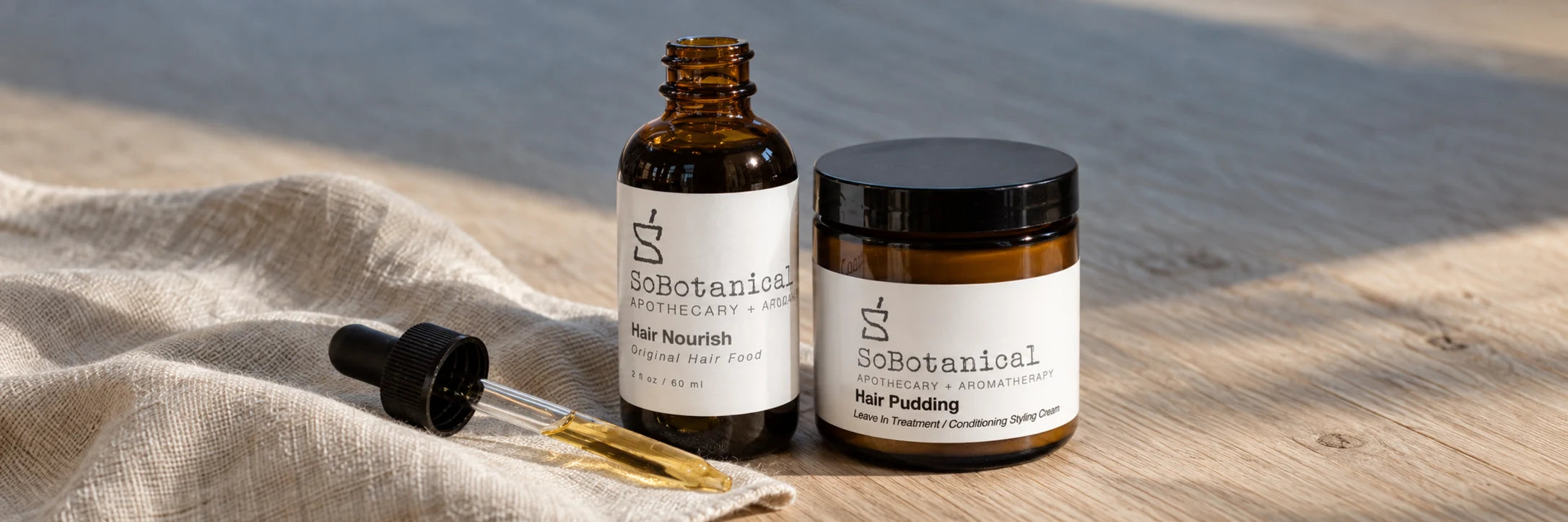 Hair Nourish and Hair Pudding with a glass dropper on linen and warm wood