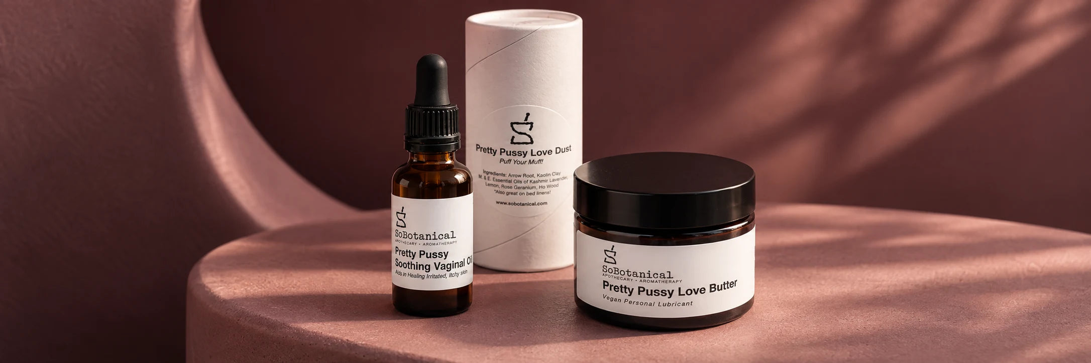 Pretty Pussy oil, Love Dust and Love Butter arranged on warm rose-colored fabric