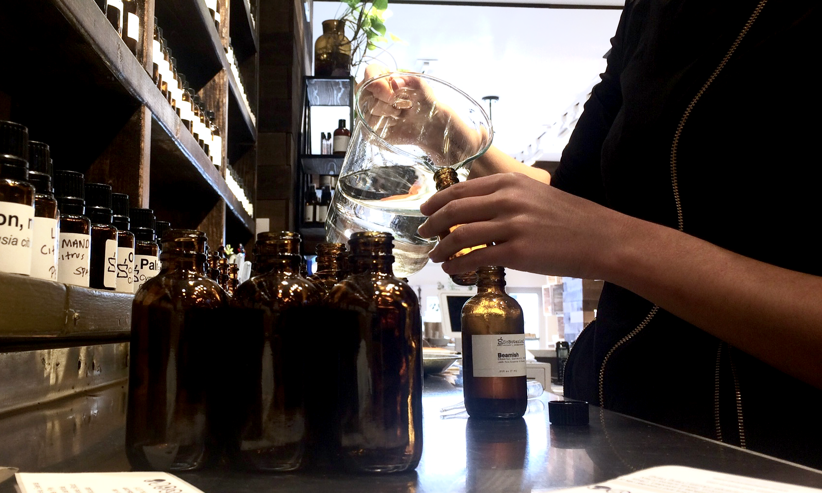 Hands pouring at the SoBotanical oil bar, surrounded by amber bottles.