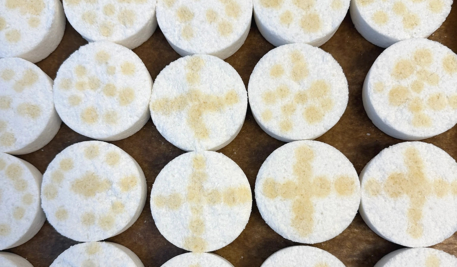 Handmade white bath bombs with pale botanical markings on a studio tray